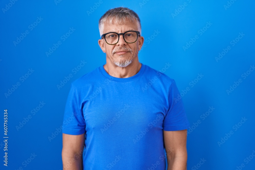 Sticker hispanic man with grey hair standing over blue background relaxed with serious expression on face. s