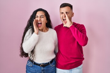 Naklejka premium Young hispanic couple standing over pink background shouting and screaming loud to side with hand on mouth. communication concept.