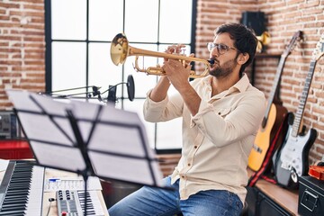 Young hispanic man musician playing trumpet at music studio