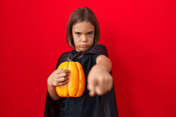 Little hispanic boy wearing a cape and holding halloween pumpkin annoyed and frustrated shouting...