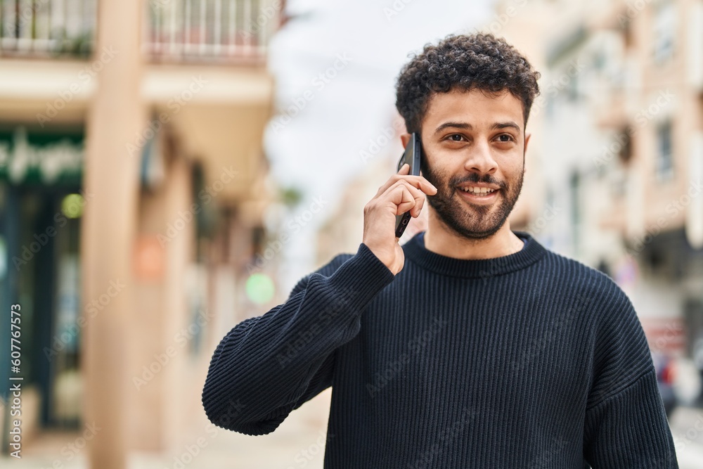 Poster Young arab man smiling confident talking on the smartphone at street