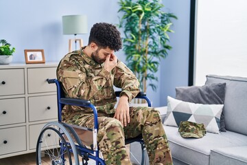 Fototapeta premium Arab man wearing camouflage army uniform sitting on wheelchair tired rubbing nose and eyes feeling fatigue and headache. stress and frustration concept.