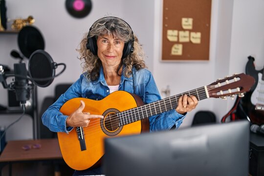 Middle age woman playing classic guitar at music studio smiling happy pointing with hand and finger