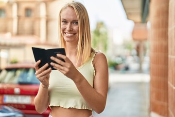 Young blonde woman smiling confident reading canada passport at street