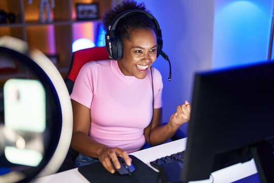 African american woman streamer playing video game with winner expression at gaming room