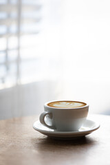 Cup of hot latte on table by white curtain window in morning