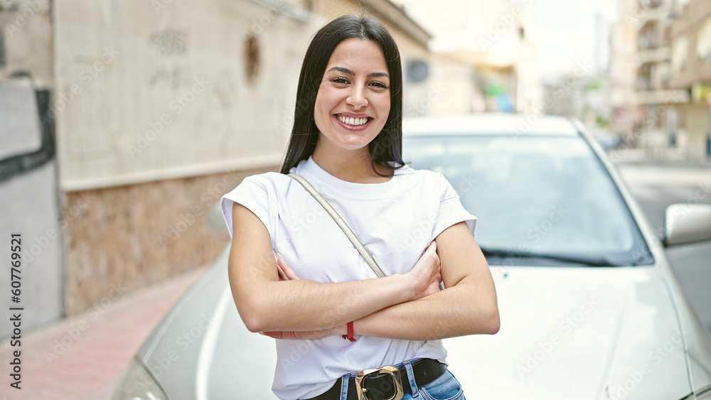 Wall mural Young beautiful hispanic woman smiling confident standing with arms crossed gesture by car at street