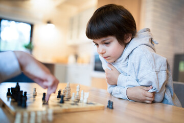 Little adorable boy playing chess at home