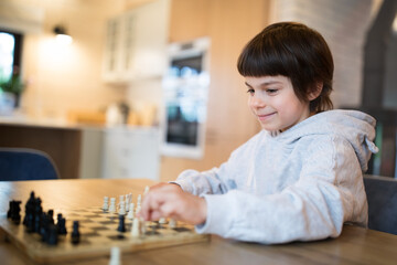 Little adorable smiling boy playing chess at home