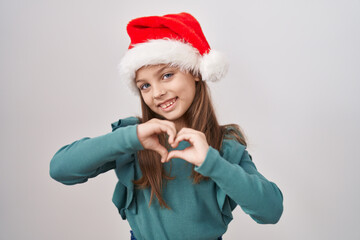 Little caucasian girl wearing christmas hat smiling in love doing heart symbol shape with hands. romantic concept.