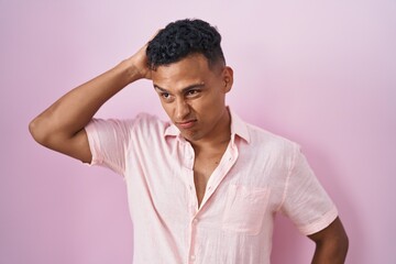 Young hispanic man standing over pink background confuse and wondering about question. uncertain with doubt, thinking with hand on head. pensive concept.