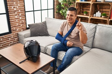Obraz premium Hispanic young man wearing arm on sling for motorbike accident surprised with an idea or question pointing finger with happy face, number one