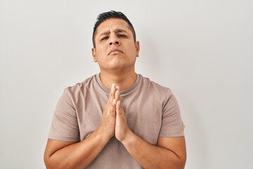 Hispanic young man standing over white background begging and praying with hands together with hope expression on face very emotional and worried. begging.