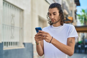 Young hispanic man using smartphone with serious expression at street