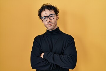 Obraz premium Hispanic man standing over yellow background skeptic and nervous, disapproving expression on face with crossed arms. negative person.