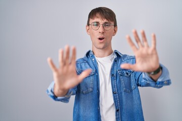 Caucasian blond man standing wearing glasses doing stop gesture with hands palms, angry and frustration expression
