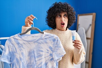 Young brunette woman with curly hair dyeing tye die t shirt angry and mad screaming frustrated and furious, shouting with anger. rage and aggressive concept.