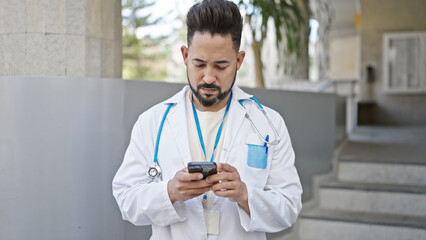 Young latin man doctor using smartphone at hospital