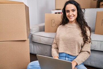 Young hispanic woman using laptop sitting on floor at new home