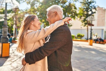 Middle age man and woman couple hugging each other standing at park