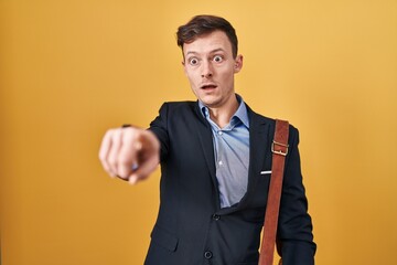Caucasian business man over yellow background pointing with finger surprised ahead, open mouth amazed expression, something on the front