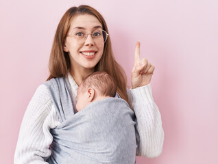 Young caucasian woman holding and carrying baby on a sling surprised with an idea or question...