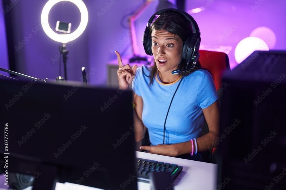 Poster Brunette young woman playing video games pointing finger up with successful idea. exited and happy. number one.