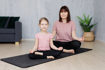 Fototapeta na wymiar family and sport concept - young mother and little daughter doing yoga together at home