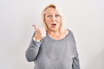 Middle age caucasian woman standing over white background surprised pointing with hand finger to the side, open mouth amazed expression.