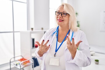 Middle age blonde woman wearing doctor uniform speaking at clinic