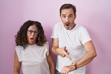 Middle age hispanic couple together over pink background in hurry pointing to watch time, impatience, upset and angry for deadline delay