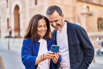 Middle age man and woman couple using smartphone standing together at street