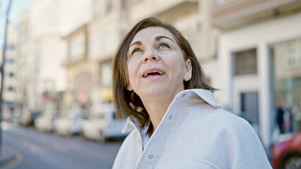 Middle age hispanic woman smiling confident looking at the sky at street