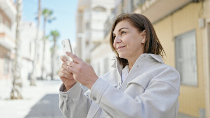 Middle age hispanic woman smiling confident make photo with smartphone at street