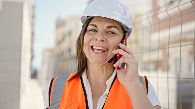 Middle age hispanic woman builder talking on smartphone at construction place