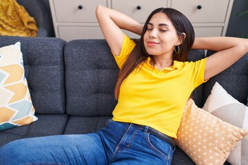 Young beautiful arab woman relaxed with hands on head sitting on sofa at home