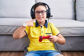 Young hispanic kid playing video game holding controller wearing headphones smiling cheerful...
