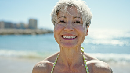Middle age blonde woman tourist wearing bikini smiling confident at the beach