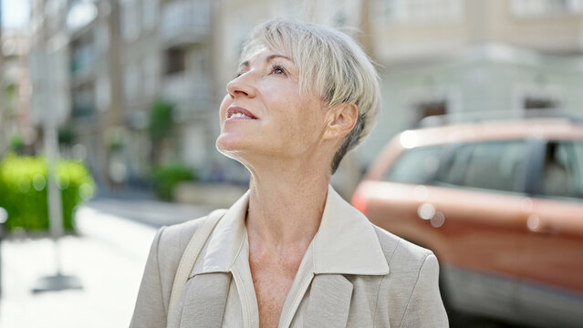 Middle age blonde woman smiling confident looking to the sky at street