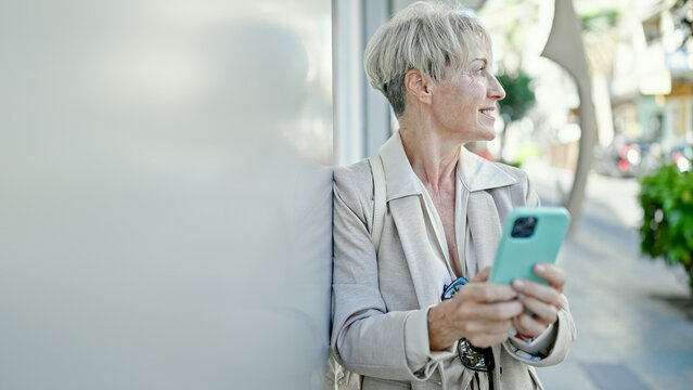 Middle age blonde woman smiling confident using smartphone at street