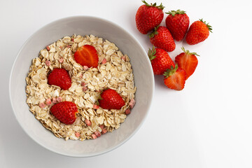 Fresh healthy breakfast of oatmeal and cereal with strawberries in a blue bowl on a white background isolate