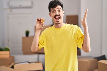 Hispanic man holding bitcoin at new home angry and mad screaming frustrated and furious, shouting with anger. rage and aggressive concept.