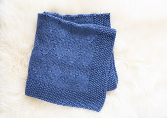 Navy blue wool knitted blanket in harlequin knitting pattern on a white furry background