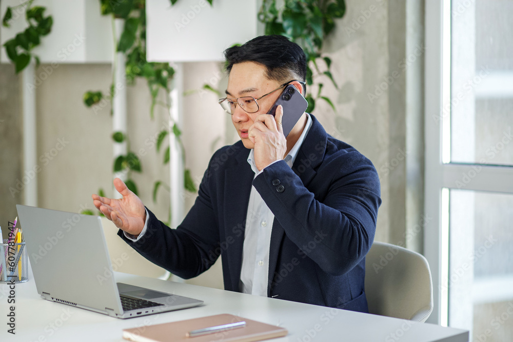 Wall mural Asian businessman working in office, using laptop and smartphone. Human resources.