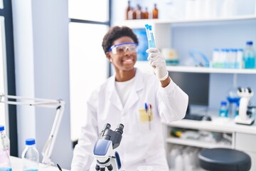 African american woman wearing scientist uniform write on clipboard holding test tubes at laboratory