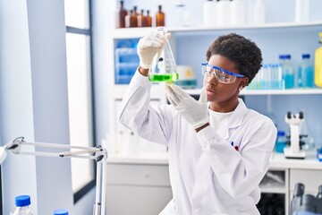 Fototapeta premium African american woman wearing scientist uniform measuring liquid at laboratory