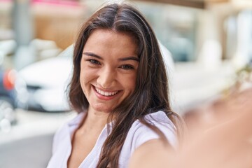 Young hispanic woman smiling confident making selfie by the camera at street