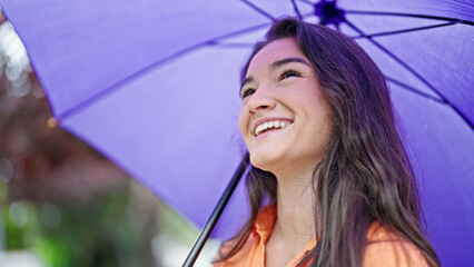 Young beautiful hispanic woman smiling confident holding umbrella at park