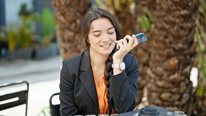 Young beautiful hispanic woman business worker sending voice message by smartphone smiling at coffee shop terrace