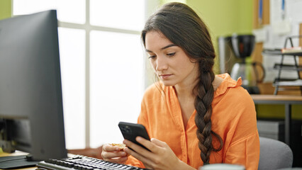 Young beautiful hispanic woman business worker having breakfast using smartphone at office